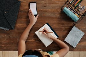 girl using smartphone writing in notebook