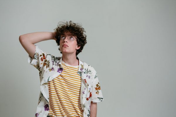 man in a floral polo thinking while his hand is on his head