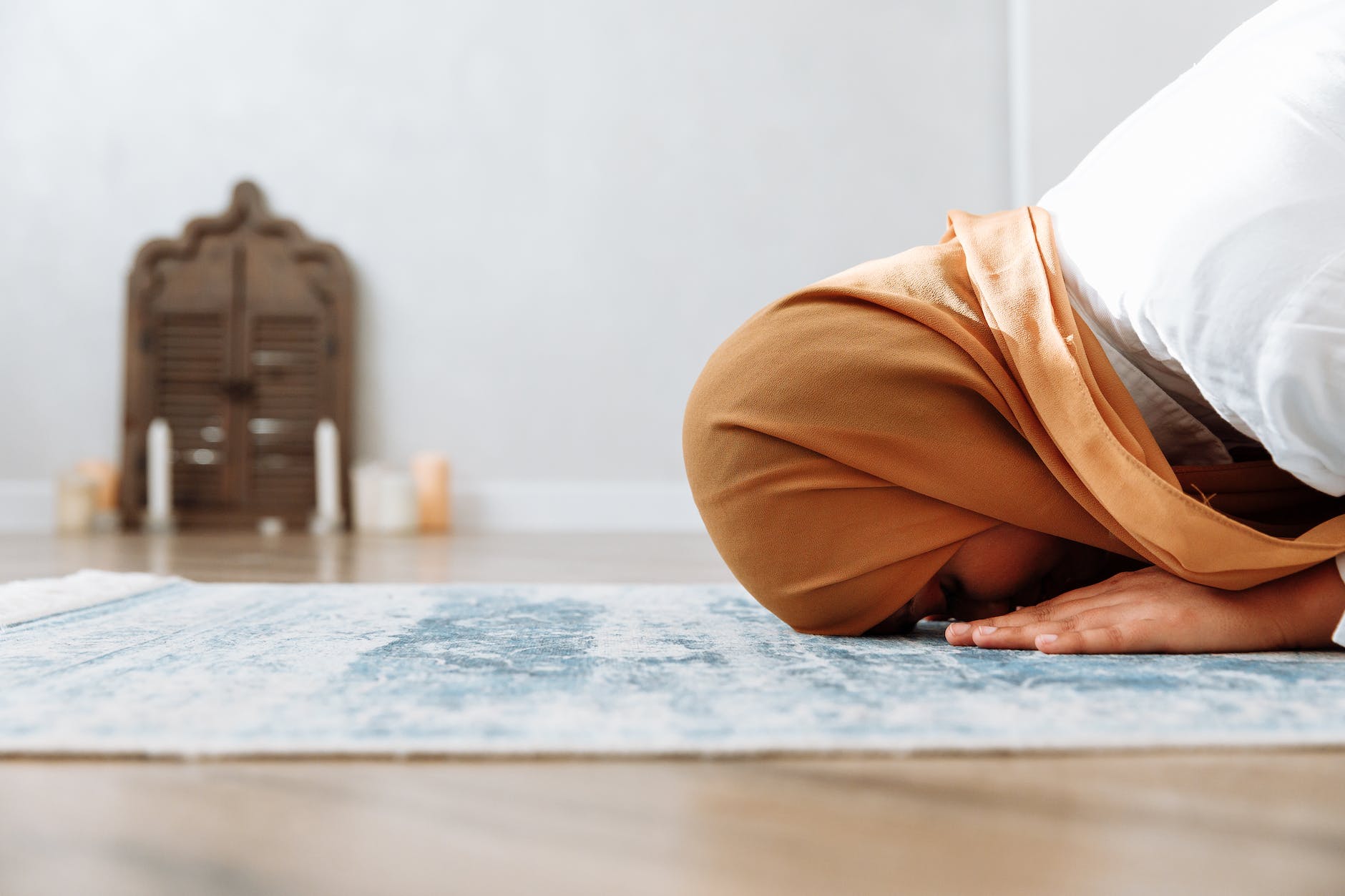 woman in brown hijab kneeling on a prayer rug