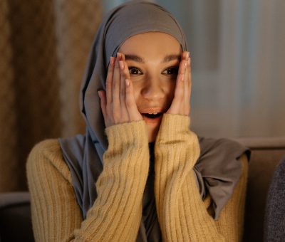 woman in gray hijab covering her face with her hands
