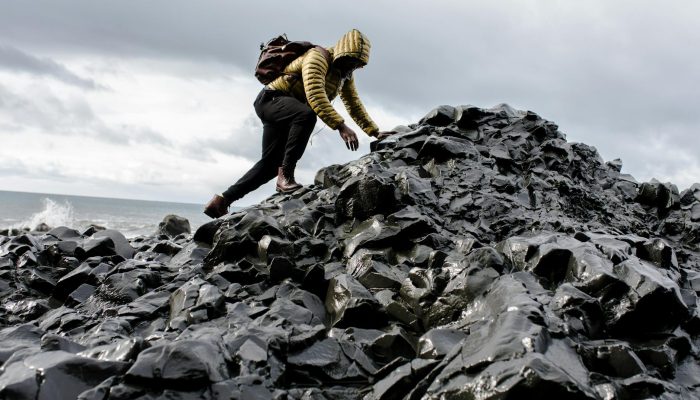 man wearing hoodie and black pants climbing up pile of rocks