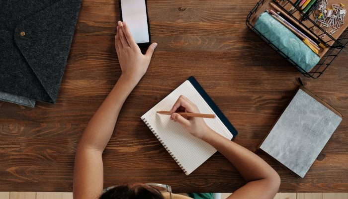 girl using smartphone writing in notebook