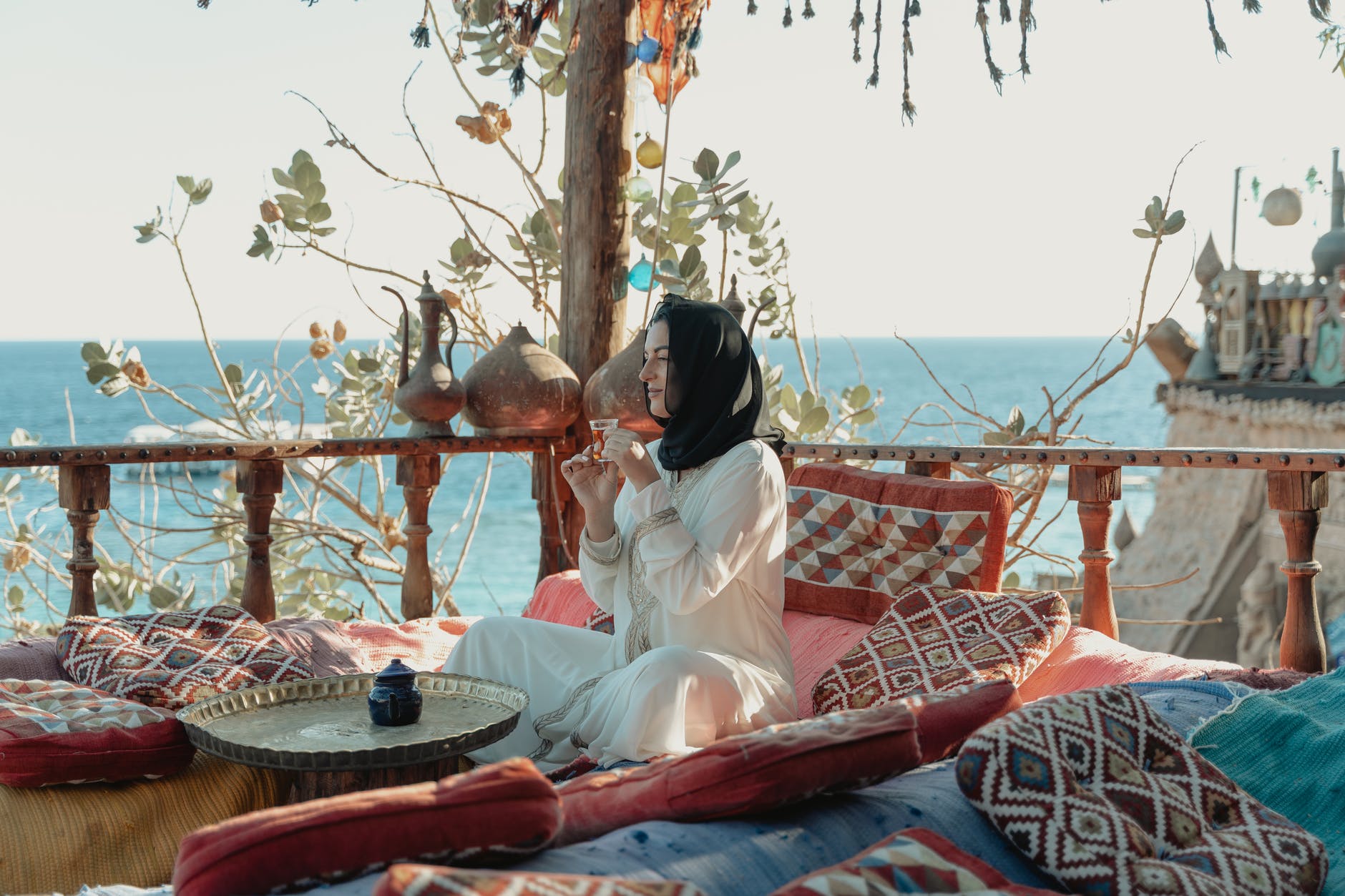 woman in white abaya and black hijab sitting with view of the sea
