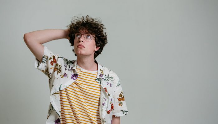 man in a floral polo thinking while his hand is on his head