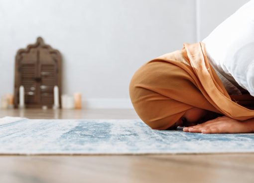 woman in brown hijab kneeling on a prayer rug