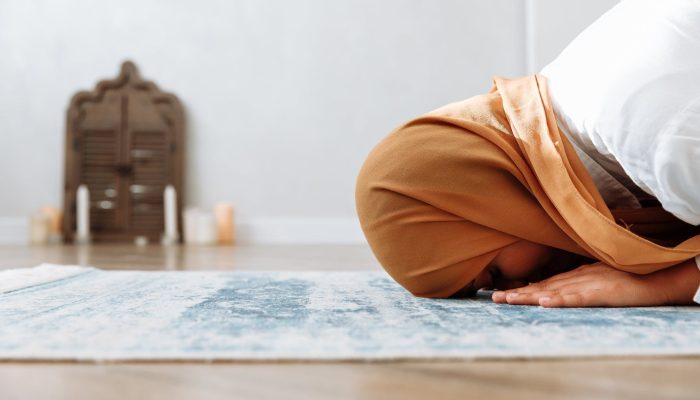 woman in brown hijab kneeling on a prayer rug