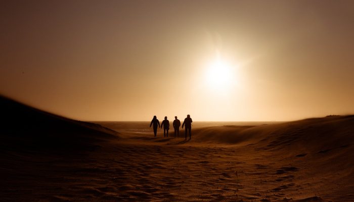 silhouette of people walking on sand dune
