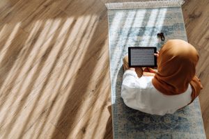 high angle shot of woman in brown hijab reading quran on a tablet