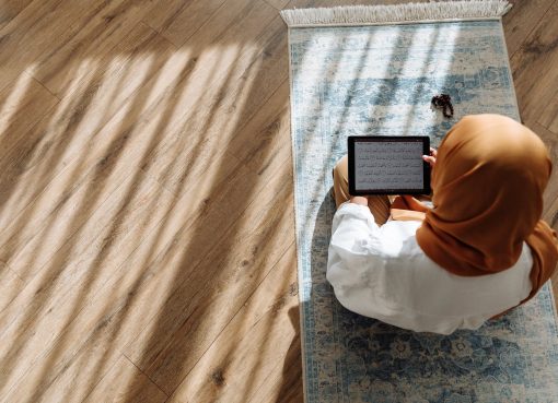 high angle shot of woman in brown hijab reading quran on a tablet